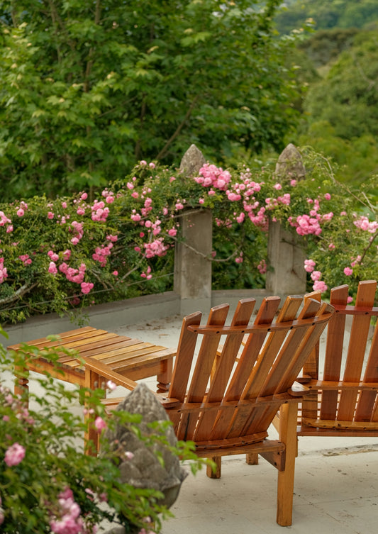 Wooden chairs and table on a patio with pink roses.
